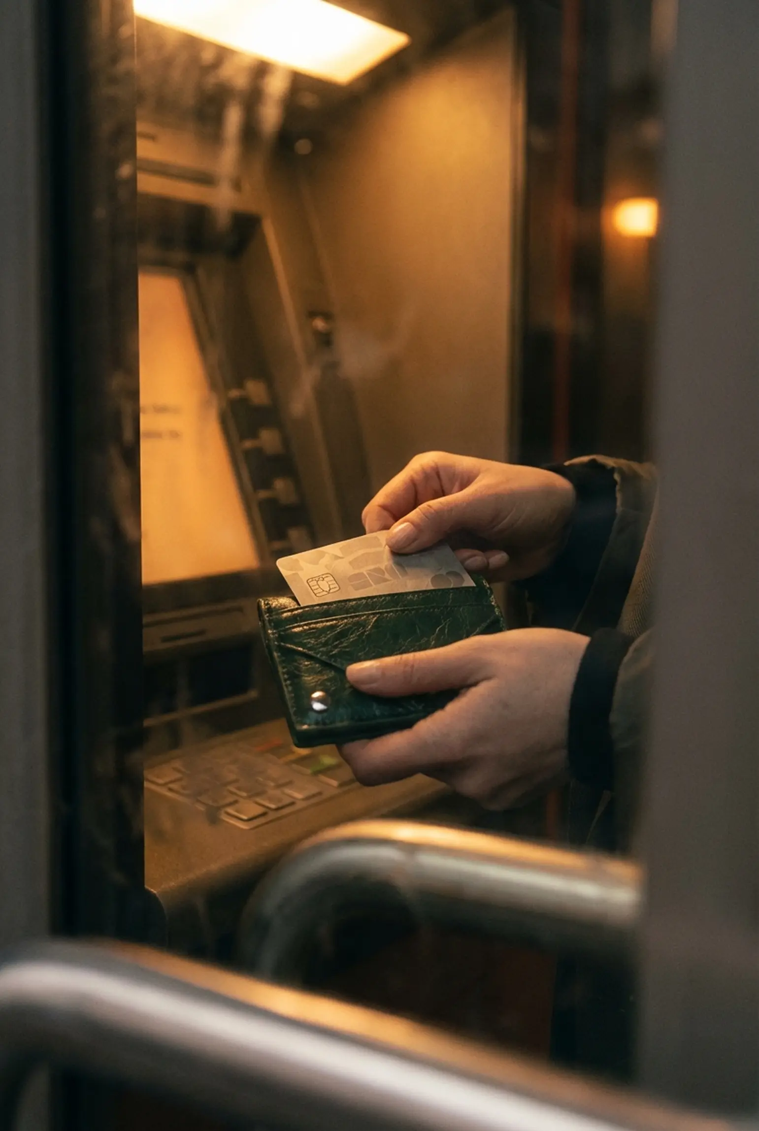 Pessoa segurando cartão e carteira em frente a um caixa eletrônico, representando saque no exterior, uso de cartão internacional e gestão prática de dinheiro em viagens internacionais.