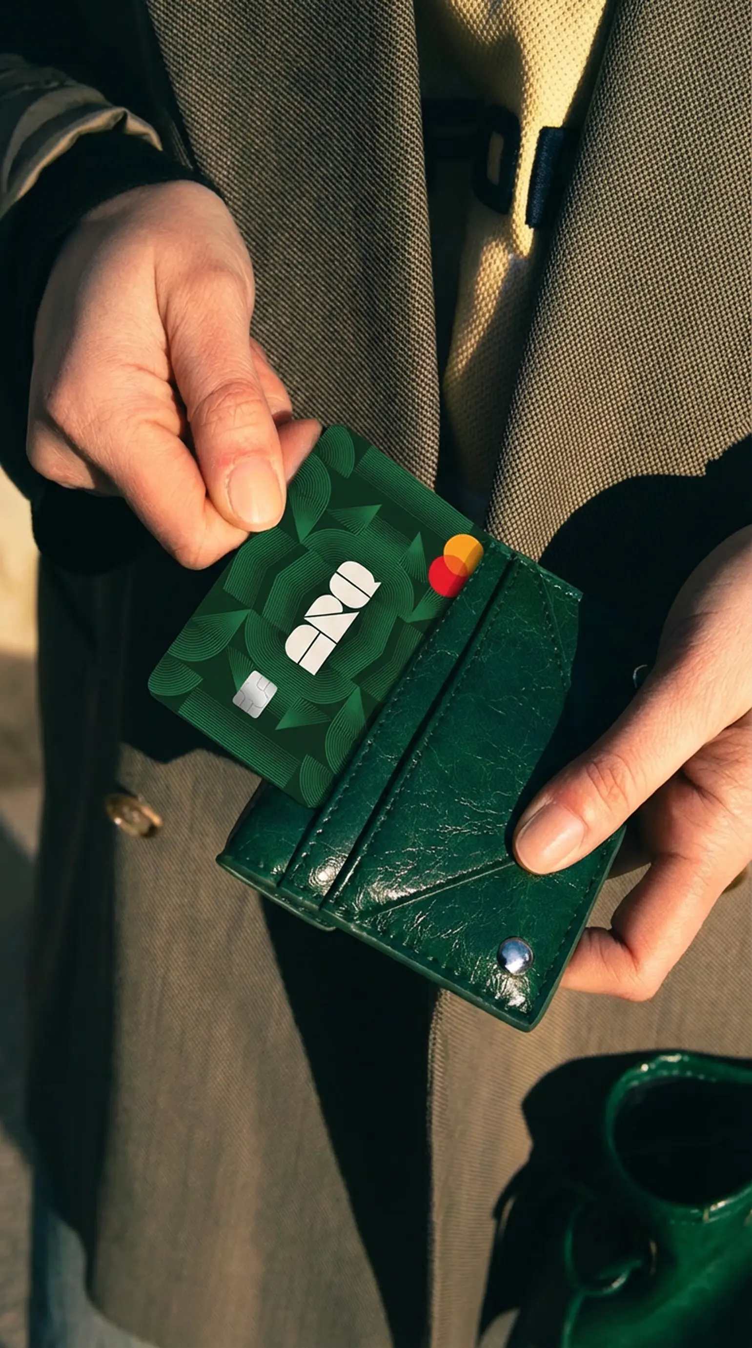 Pessoa segurando um cartão verde e uma carteira, representando praticidade para pagamentos internacionais, organização financeira e uso de cartão em viagens.