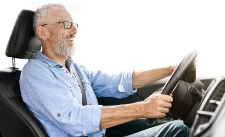 Senhor de cabelos grisalhos sorrindo ao volante enquanto dirige seu carro em um trajeto do dia a dia