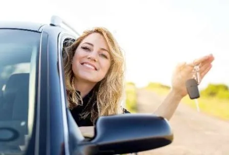 Mulher sorrindo na janela do carro segurando a chave em uma estrada, pronta para uma viagem