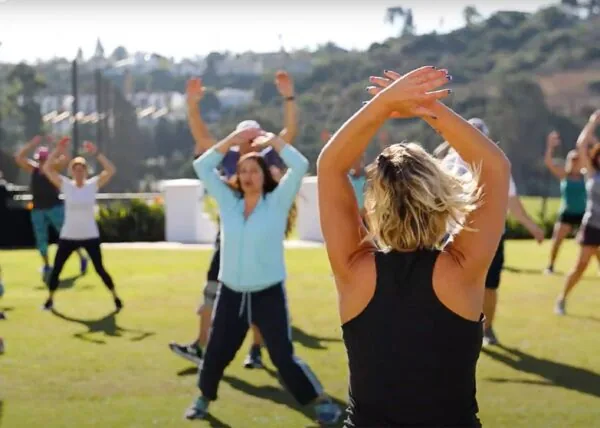 A group of adults doing jumping jacks together on a green resort lawn.
