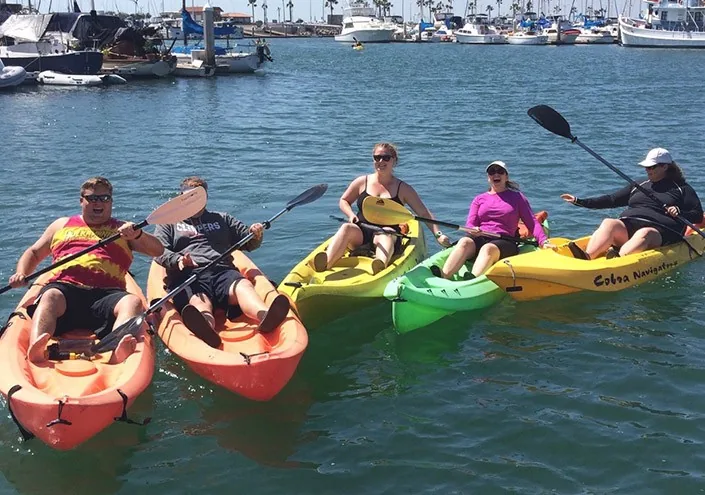 A small group paddles kayaks together on calm harbor water.