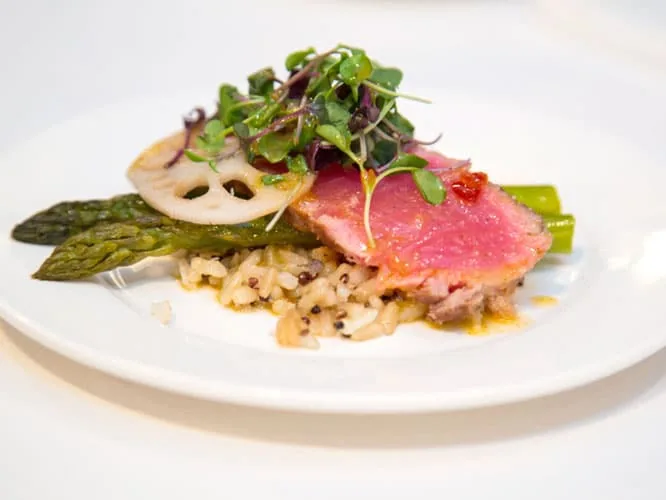 A plated dish of seared tuna with asparagus, grains and microgreens on a white plate.