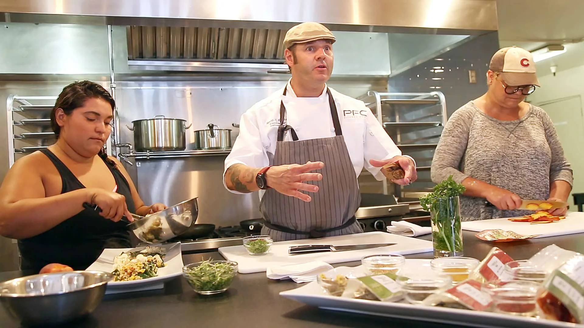 A wellness chef leads two clients through a hands-on cooking demonstration in a kitchen.