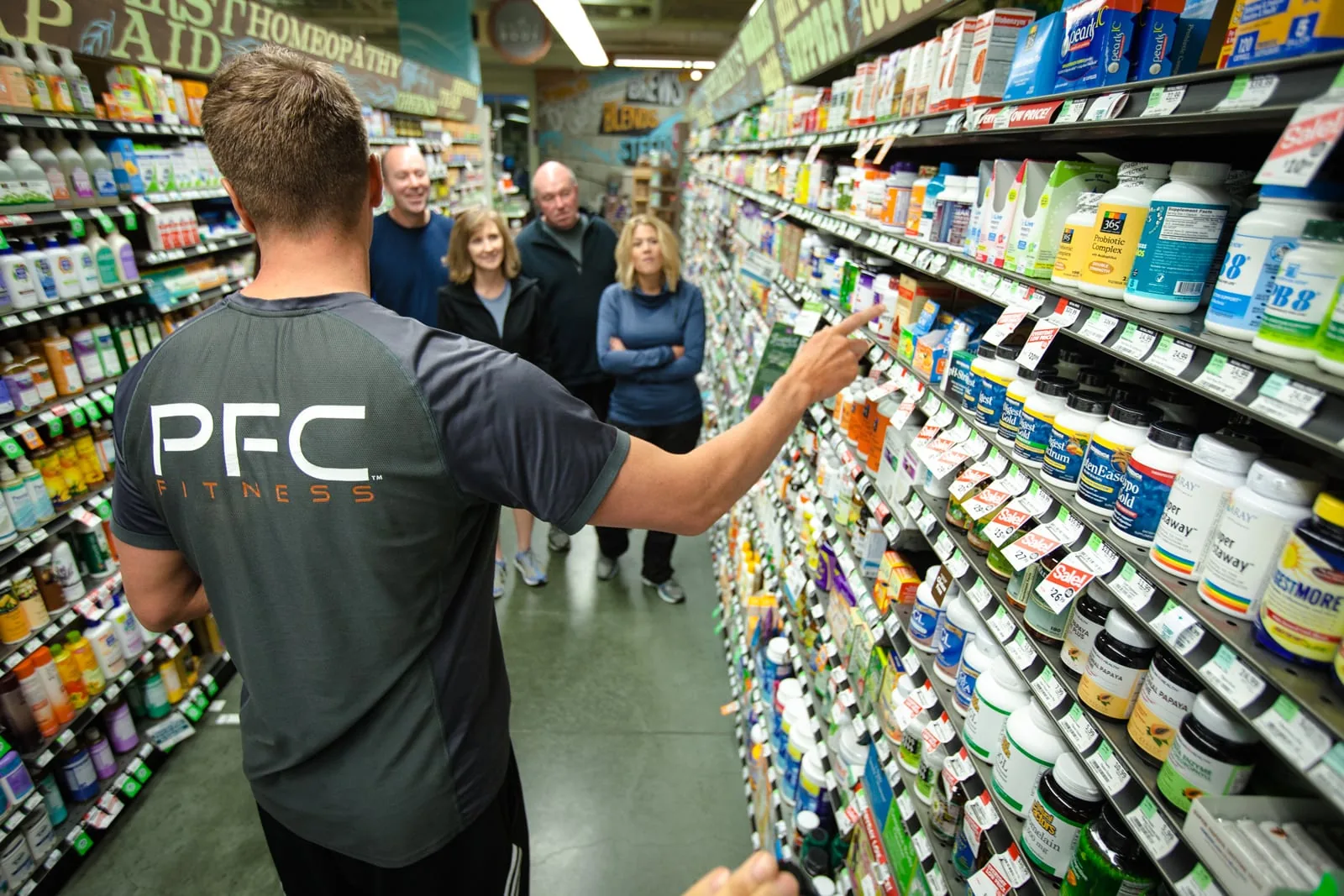 A trainer in a PFC shirt guides a group through a grocery store aisle.