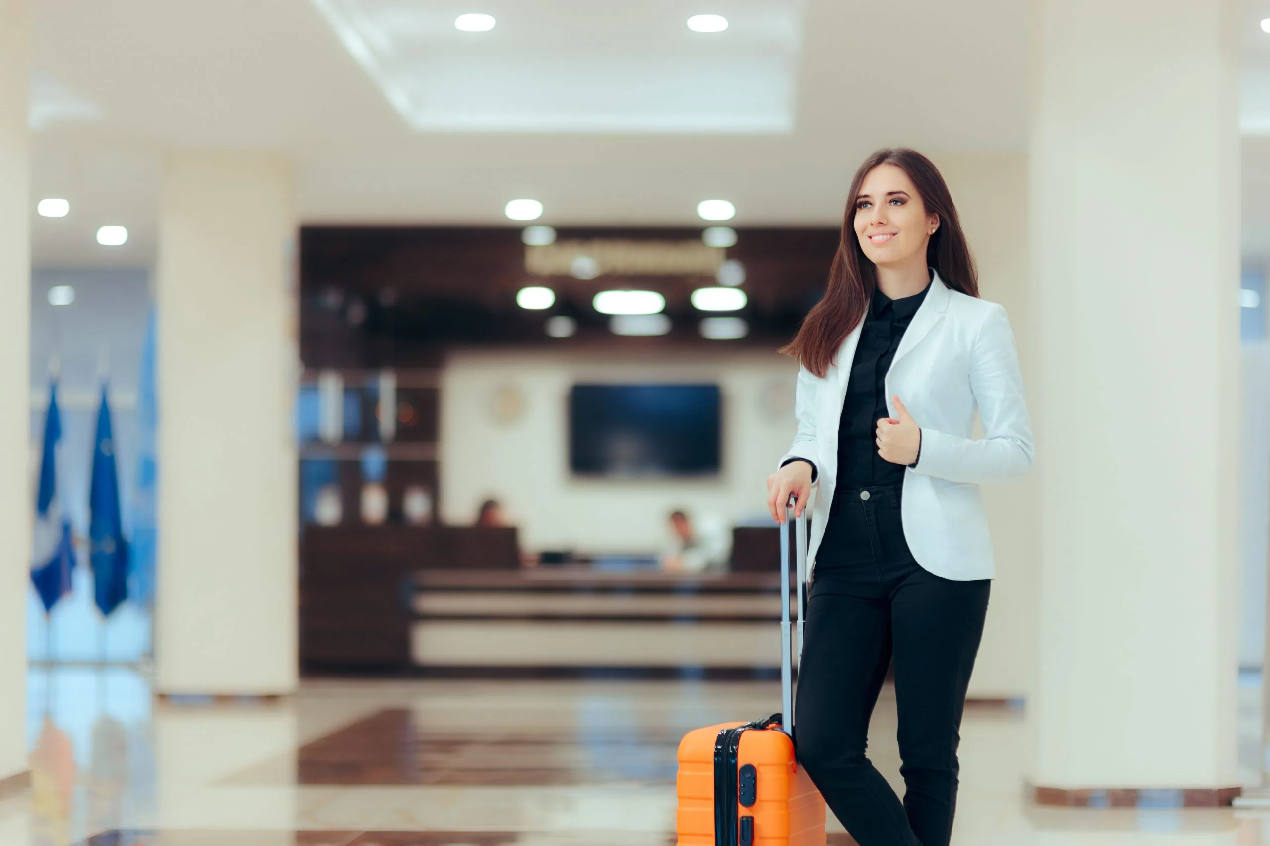 A businesswoman arrives in a hotel lobby wheeling a suitcase.