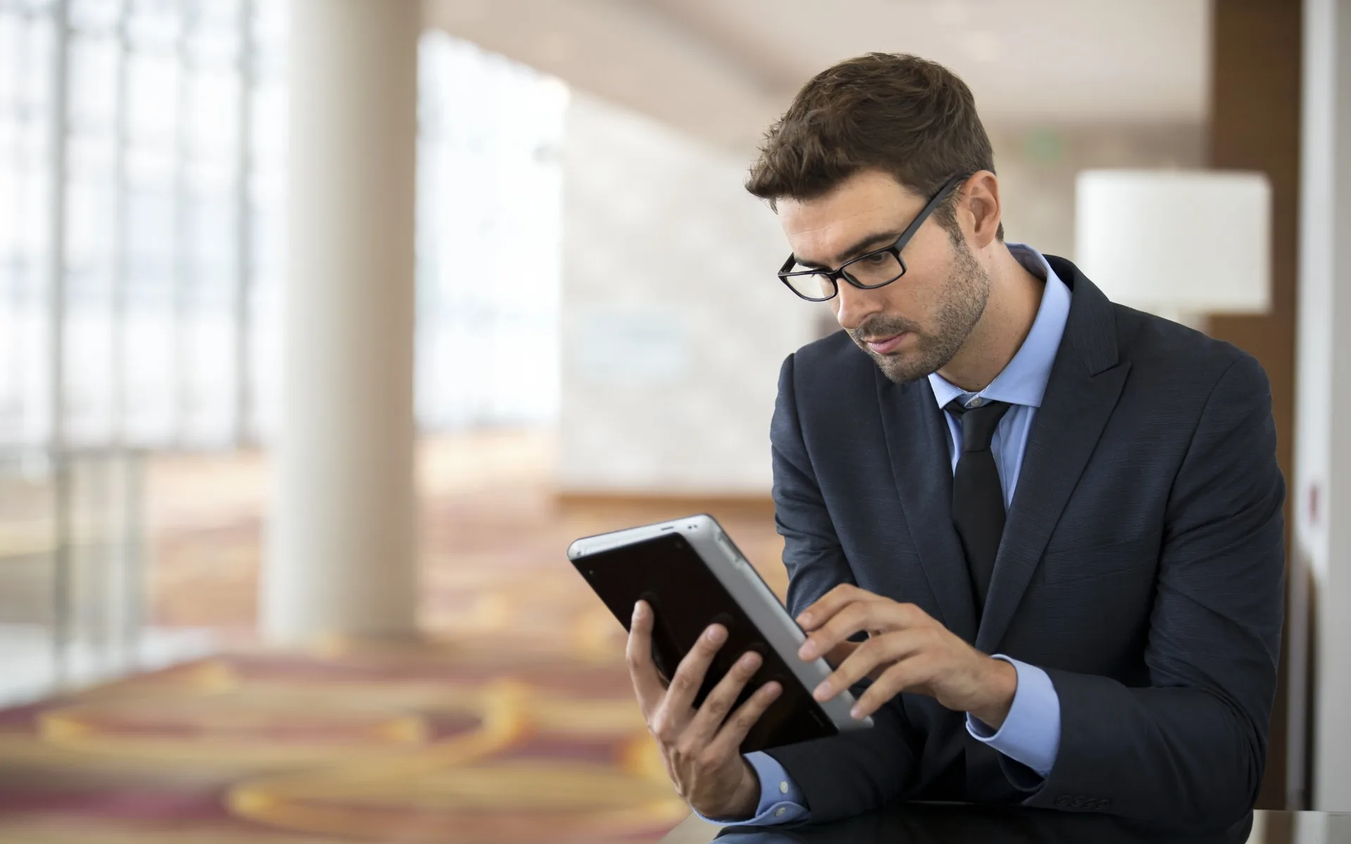 A hotel manager reviews data on a tablet in a bright hotel lobby.