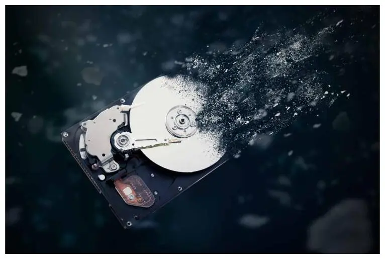 A hard drive dissolving into particles against a dark background.
