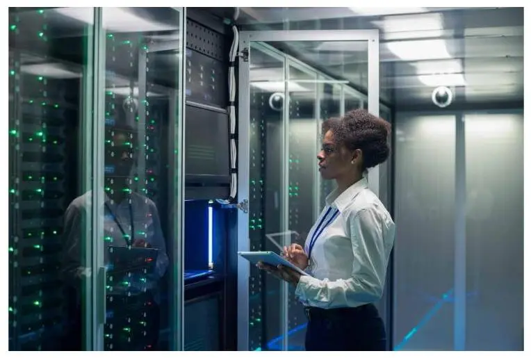 A technician with a tablet inspects server racks in a data center.