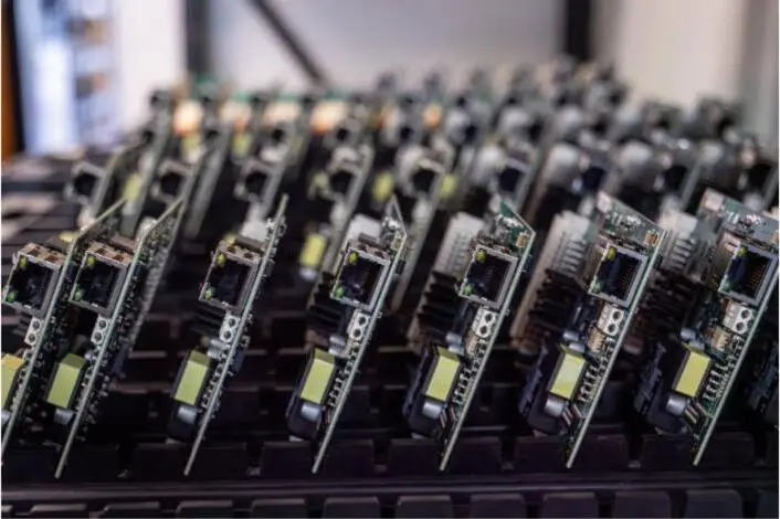 Rows of circuit boards seated in a test rack under bright light.