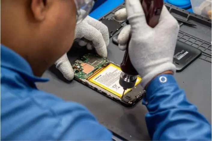 A technician in gloves repairs the internals of a smartphone at a bench.