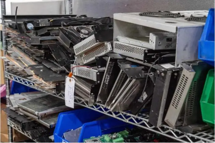 Used server and networking hardware stacked on wire shelving with an inventory tag.