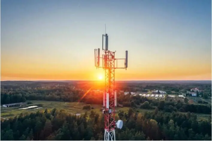 A cellular communications tower silhouetted against a sunset over open country.