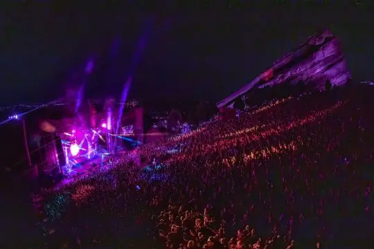 A packed outdoor amphitheatre crowd at night lit by stage lights.