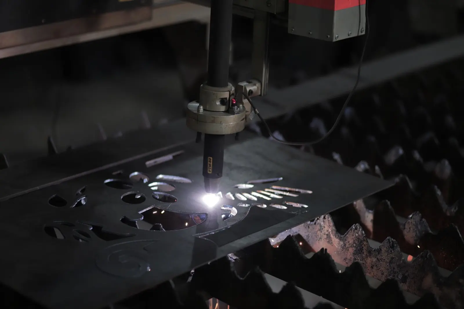 Laser cutting head cutting a flat metal sheet with sparks in a dark workshop