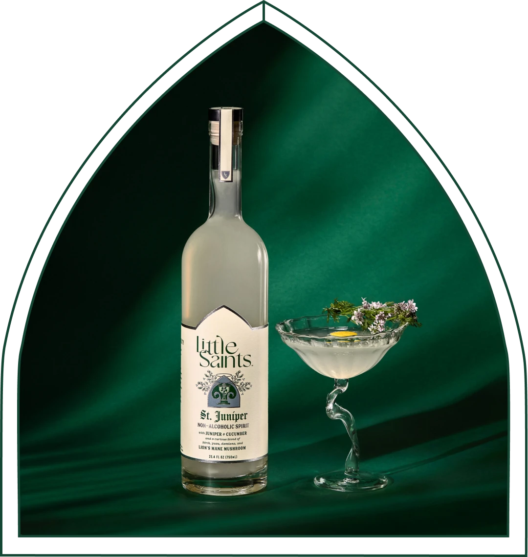 The Little Saints St. Juniper non-alcoholic gin bottle beside a martini on green marble.